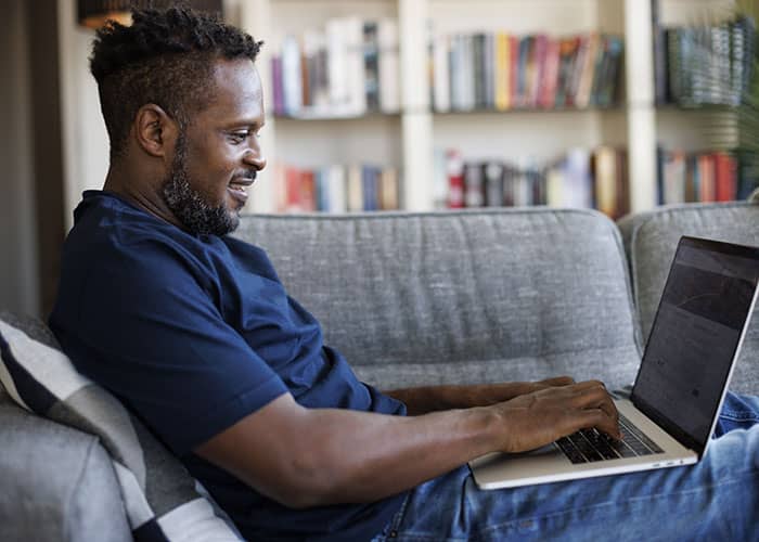 Man working on laptop while sitting on the couch and smiling